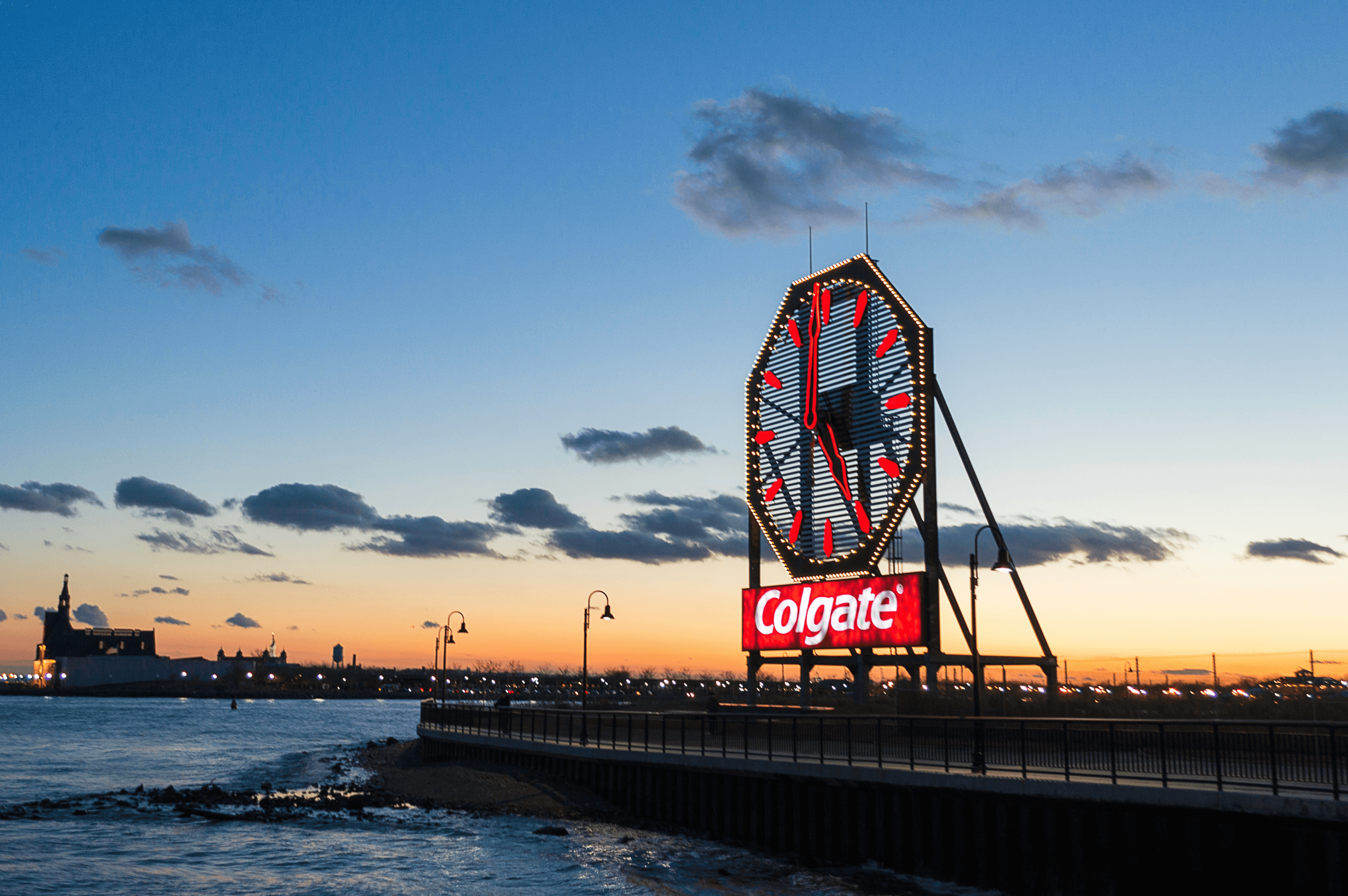 The giant, illuminated Colgate Clock landmark on a waterfront pier at sunset.
