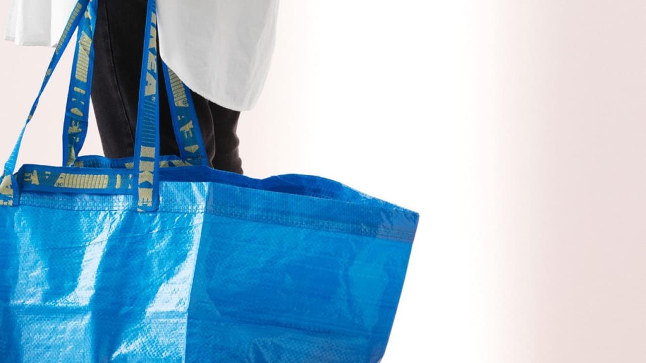 A person carrying a large, blue IKEA reusable shopping bag.