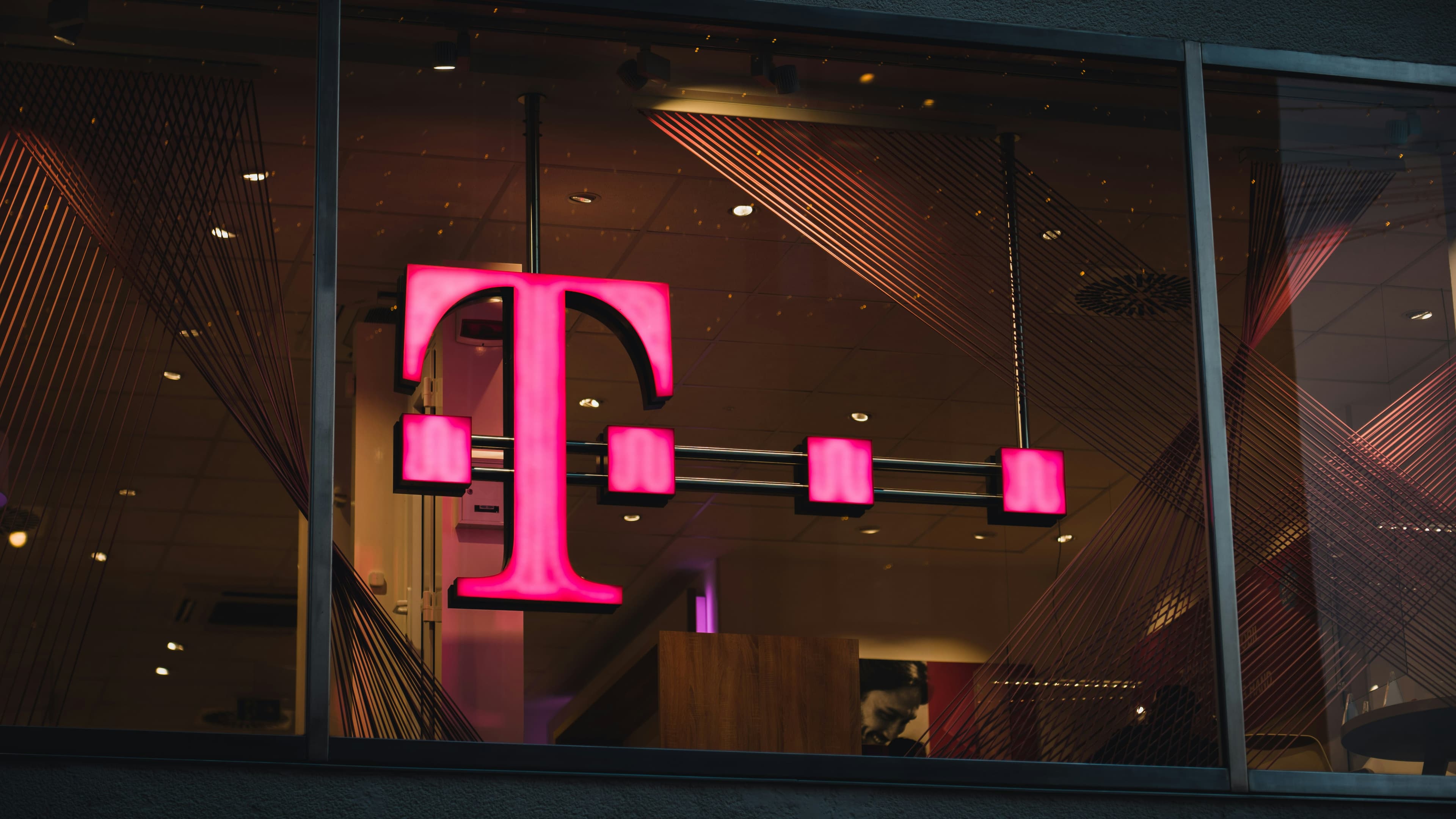 An illuminated magenta T-Mobile logo inside a retail store window.